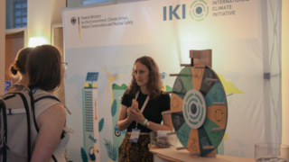 Messestand mit zwei Personen vor einem Glücksrad und einem Banner mit Logos im Hintergrund