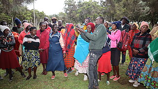 Group of people in colorful clothing standing outdoors around a man who is speaking and gesturing