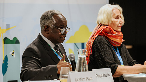 Two people side by side, one holding a microphone.