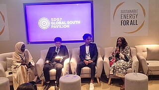 Four individuals sit on stage for a panel discussion. Behind them, a screen displays "SDG7 Global South Pavilion," alongside a sign reading "Sustainable Energy for All."