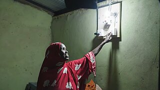 Person in rotem Kleid schaltet Lichtschalter an einer Wand in einem dunklen Raum ein