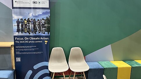 Roll-up-Banner zum Fotowettbewerb 2025 der IKI neben zwei Designerstühlen und bunten Sitzwürfeln.