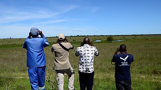 Eine Gruppe von Menschen steht in einem offenen Feld und scheint etwas zu beobachten.