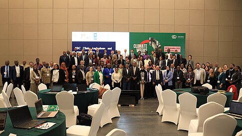 Teilnehmende posieren in einem Konferenzraum mit Tischen und Stühlen für ein Gruppenfoto.