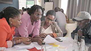 Vier Personen sitzen mit Papieren an einem Tisch und diskutieren. 