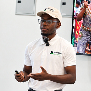 Ein junger Unternehmer in Sambia trägt ein weißes Polohemd und eine weiße Kappe mit dem Logo von Umodoro Biotechnology und präsentiert vor einem Bildschirm mit einer PowerPoint-Folie zu Biogas für den sambischen Markt.