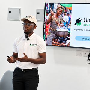 Ein junger Unternehmer in Sambia trägt ein weißes Polohemd und eine weiße Kappe mit dem Logo von Umodoro Biotechnology und präsentiert vor einem Bildschirm mit einer PowerPoint-Folie zu Biogas für den sambischen Markt.