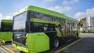 A sleek green-and-black electric bus parked beside others in an urban setting.