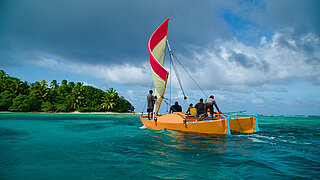 A catamaran sailing in the ocean, led by a group of people coming together for a community-based conservation effort.