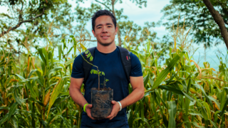 A black haired man holds a seedling.