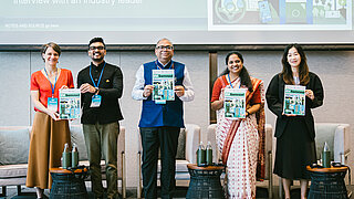 Gruppenfoto von fünf Konferenzteilnehmern, die auf einer Veranstaltung Publikationen zu Elektromobilität präsentieren.