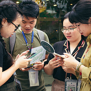4 junge Menschen stehen beieinander und schauen auf ihre Smartphones