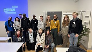 Eine Gruppe junger Menschen steht für ein Gruppenbild in einem Seminarraum. 