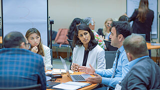 Eine Gruppe von Fachleuten führt eine Diskussion in einer Besprechung, bei der ein Laptop und Flipchart verwendet werden.