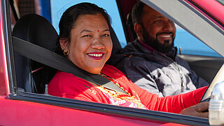 Woman wearing a red top smiling while driving a car with a man smiling in the passenger seat