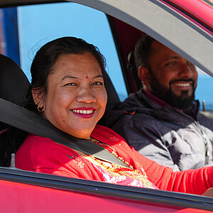 Woman wearing a red top smiling while driving a car with a man smiling in the passenger seat