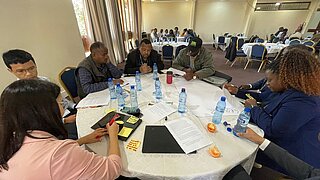 Mehrere Teilnehmende sitzen in einer kleinen Arbeitsgruppe um einen runden Tisch, schreiben Notizen und diskutieren beim Workshop der NAP Expo 2025.