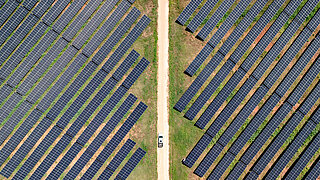 An aerial view of a solar farm, with rows of solar panels placed on the land and a car on the road crossing the middle.