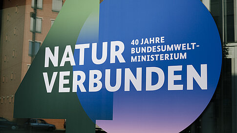 Rundliches Schild mit den Worten 'NATUR VERBUNDEN' und '40 JAHRE BUNDESUMWELT-MINISTERIUM 1986-2026'
