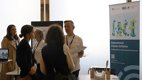 Personen stehen an einem Infostand und unterhalten sich.