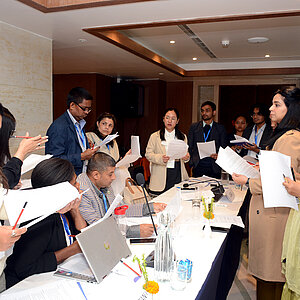 Mehrere junge Frauen und Männer gruppieren sich in einem Konferenzraum um einen Tisch herum und führen Verhandlungen.