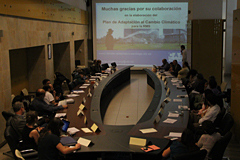 Menschengruppe sitzt an einem Konferenztisch und betrachtet eine Präsentation