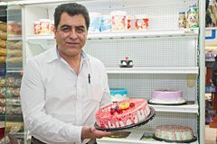 Person holding cake in front of refrigerated display cabinet