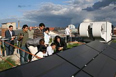 Group of people standing on roof and examining solar panel
