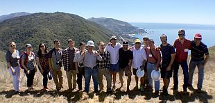 Zwei Arbeiter mit Schutzhelömen stehen auf einer Solardachanlage und säubern sie mit Wasser und Wischer.