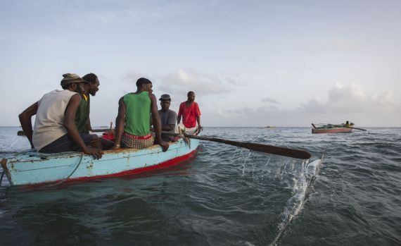Mehrere Fischer sitzen in einem kleinen Ruderboot, einer rudert. Im Hintergrund fährt ein weiteres Boot. Der traditionelle Fischfang gehört zur Lebensart der Karibikbewohner und ist ein wichtiger Wirtschaftszweig. Foto: Tim Calver.