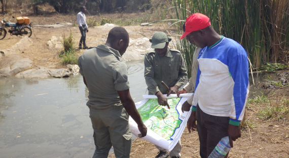 Mehrere Personen stehen an einem kleinen Tümpel um eine Karte herum und besprechen sich, bei einem Besuch vor Ort zur Überprüfung der Elemente der Zonierungskarte des Schutzgebiets Togodo. Foto: GIZ