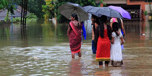 People with umbrellas wading through a flooded street.