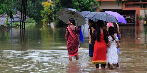 Menschen mit Regenschirmen waten durch überflutete Straße