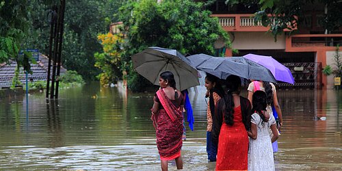 Menschen mit Regenschirmen waten durch überflutete Straße.