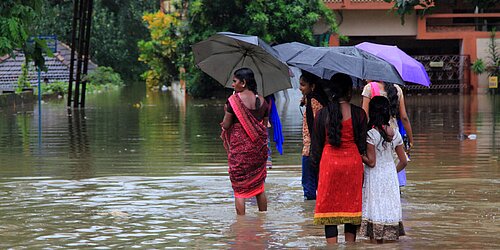 People with umbrellas wading through a flooded street.