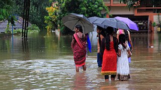 Menschen mit Regenschirmen waten durch überflutete Straße.